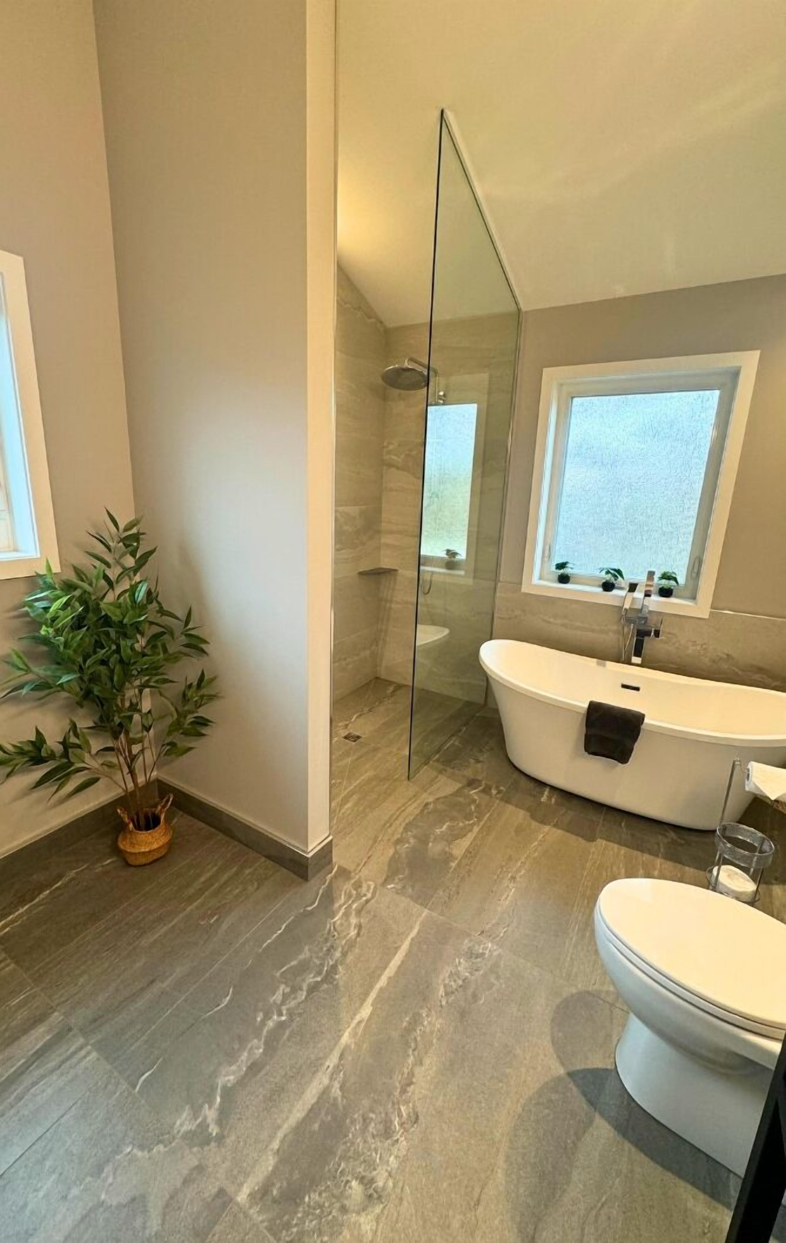 Un baño moderno con cabina de ducha de vidrio, una bañera independiente y un inodoro.