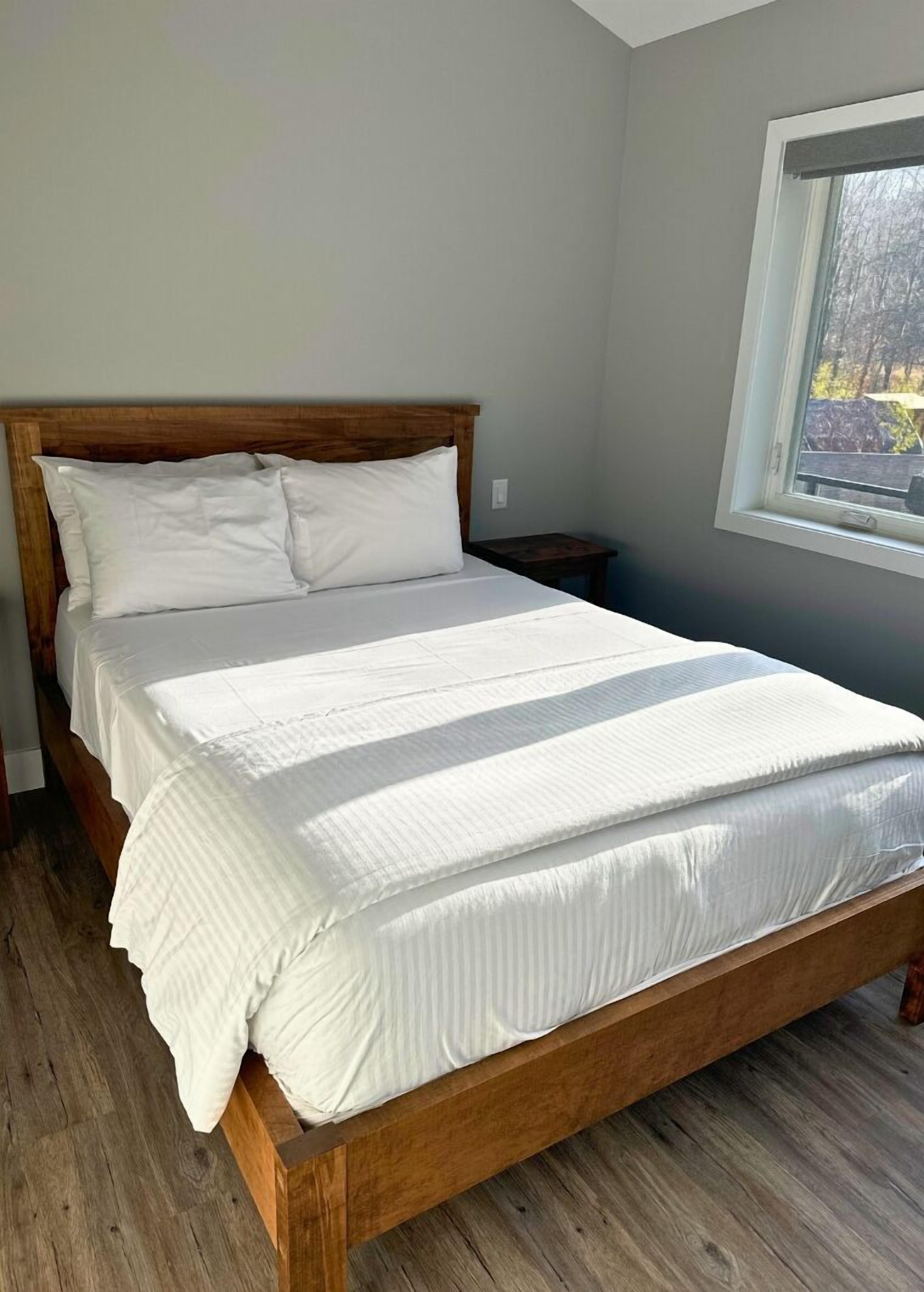 A neatly made bed in a room with a wooden headboard, a small bedside table, and a window with a view of trees.