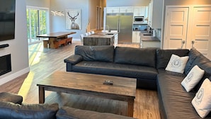 A modern living room with a large black leather sofa, a wooden coffee table, and a fireplace. - Orchard Run Chalet (The Blue Mountains)