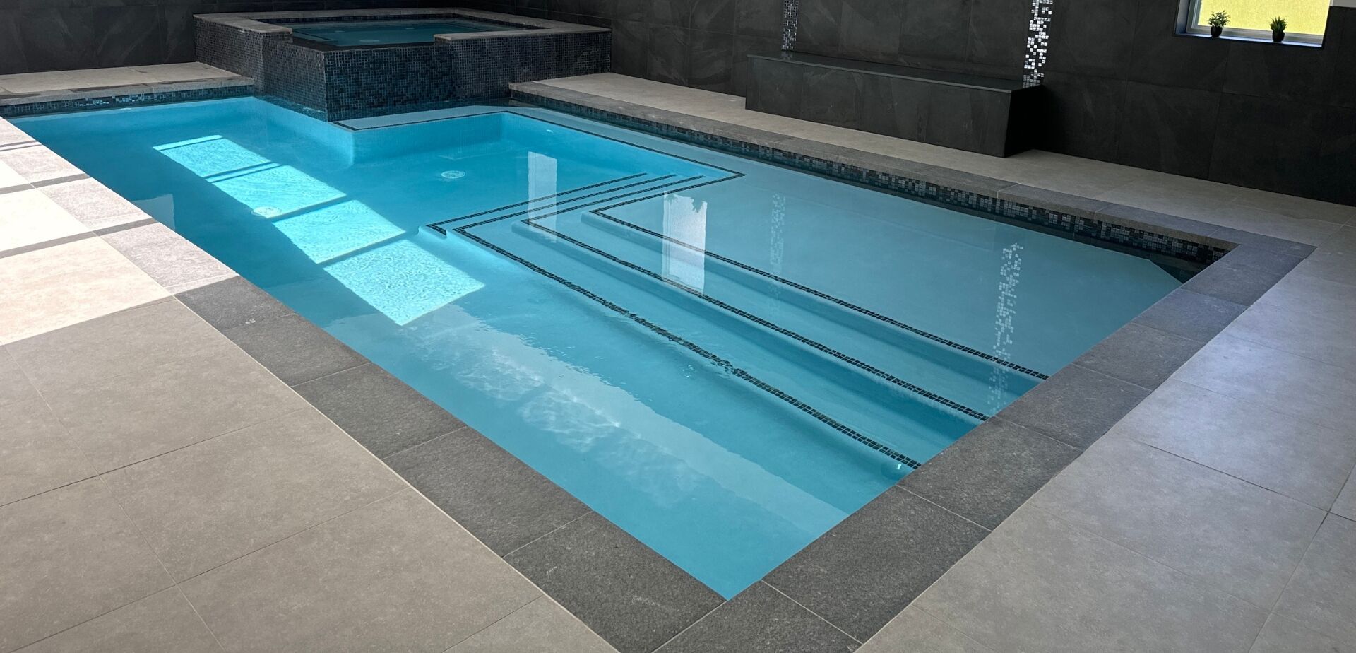 Una piscina interior moderna con carriles delimitados, suelo de baldosas y pared oscura.