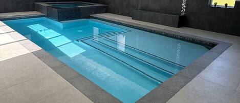 Una piscina interior moderna con carriles delimitados, suelo de baldosas y pared oscura.