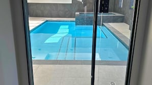 A glass door leading to a swimming pool area with a tiled floor and a spa section. - Orchard Run Chalet (The Blue Mountains)