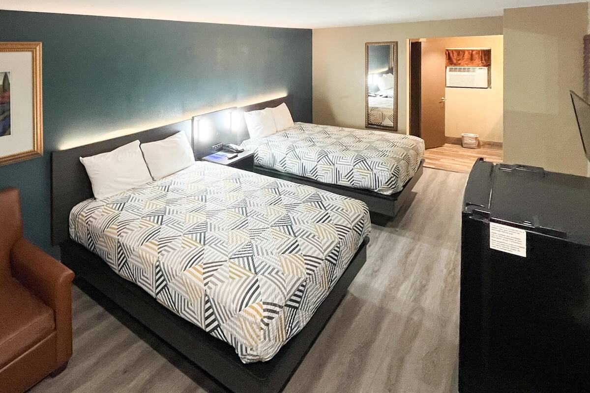 A hotel room with two beds, a brown leather chair, a desk with a phone, and a refrigerator.