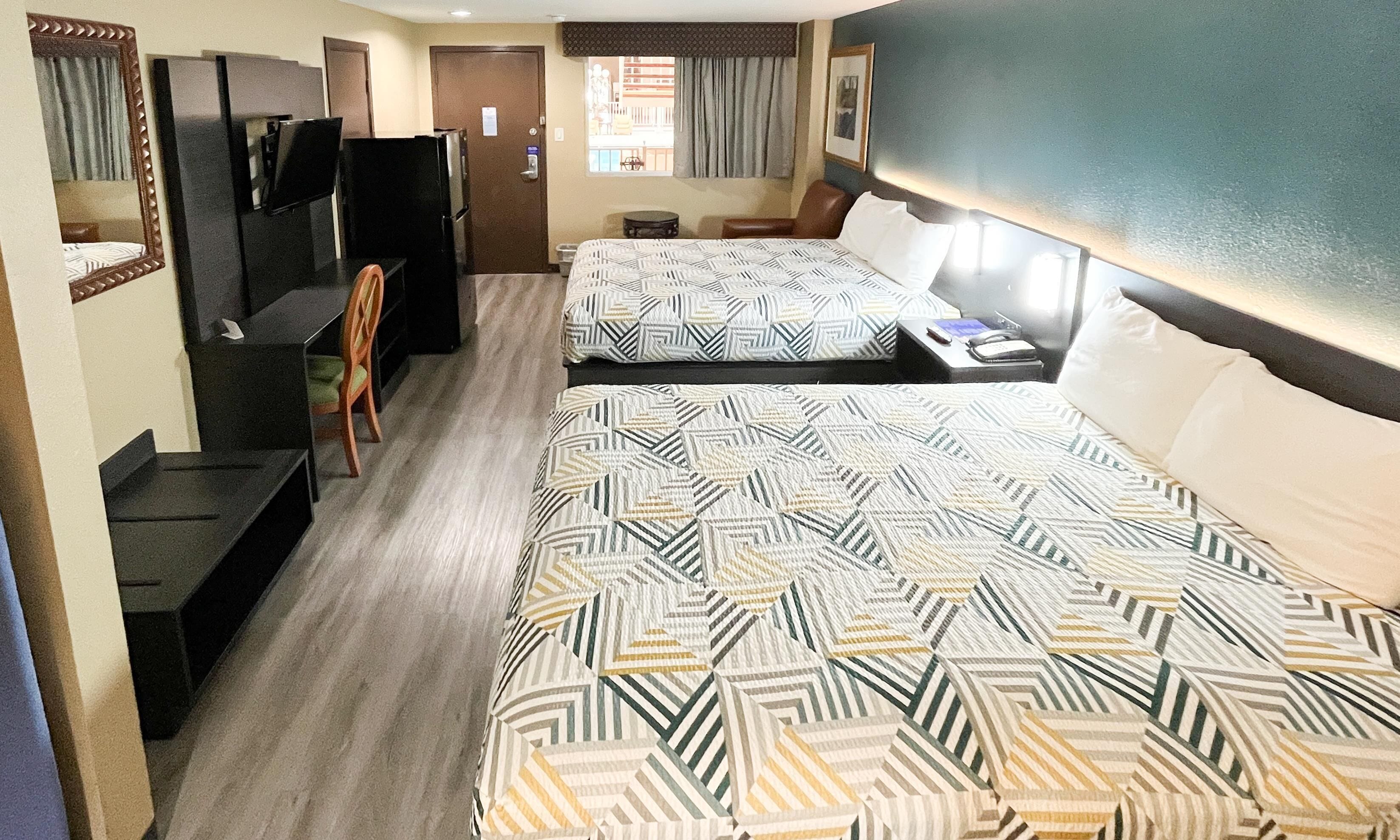 Une chambre d’hôtel avec deux lits, un bureau, une chaise, une télévision et une fenêtre avec des rideaux.