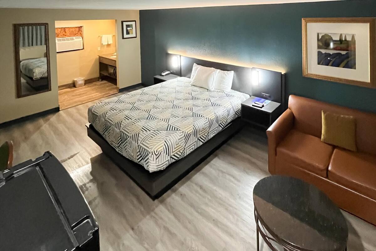 A hotel room with a bed, a brown leather sofa, a desk, and a chair.