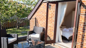 A balcony with wicker furniture and a glass table, a brick wall, and a bedroom with a bed and curtains. - Newclose Farm (Yarmouth)