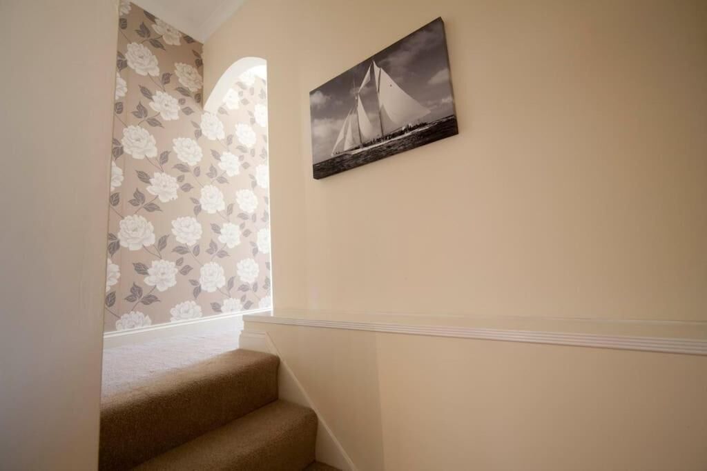 Una escalera con peldaños alfombrados que conduce a una plataforma, un estampado floral en la pared contigua y una pintura en blanco y negro de un velero en la pared.