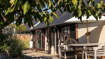 A wooden cottage with a brick exterior, a white door, and a patio with a table and chairs.