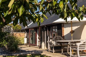 A wooden cottage with a brick exterior, a white door, and a patio with a table and chairs. - Newclose Farm (Yarmouth)
