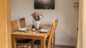 A dining table set with plates, a wine bottle, and a vase of flowers. - Newclose Farm (Yarmouth)