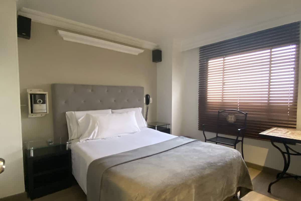 Una camera da letto con un letto, comodini, una scrivania e una finestra con persiane.
