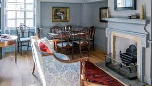 A dining room with a fireplace, a long table with chairs, and a patterned sofa.