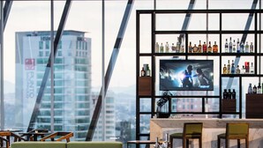 Un área de bar moderna con asientos, televisor y vista a la ciudad.