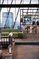 Eine moderne Bar mit Sitzgelegenheiten, einem Fernseher und Blick auf die Stadt.