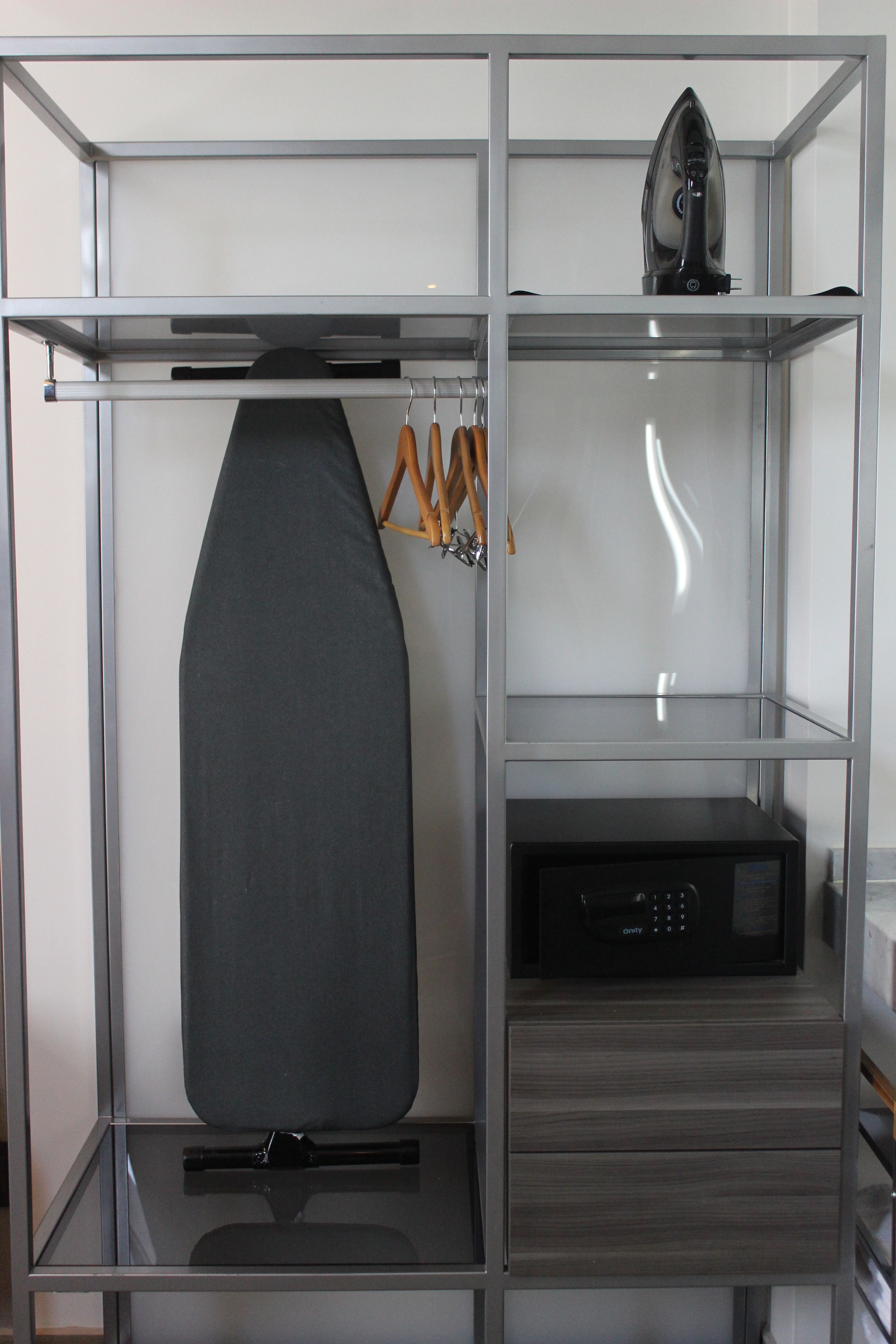 Un meuble de rangement moderne, à étagères ouvertes, avec un espace pour suspendre des vêtements, un micro-ondes et un petit tiroir.
