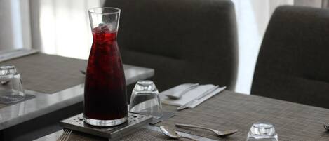 A dining table with a glass of red beverage, cutlery, and a napkin with a logo.
