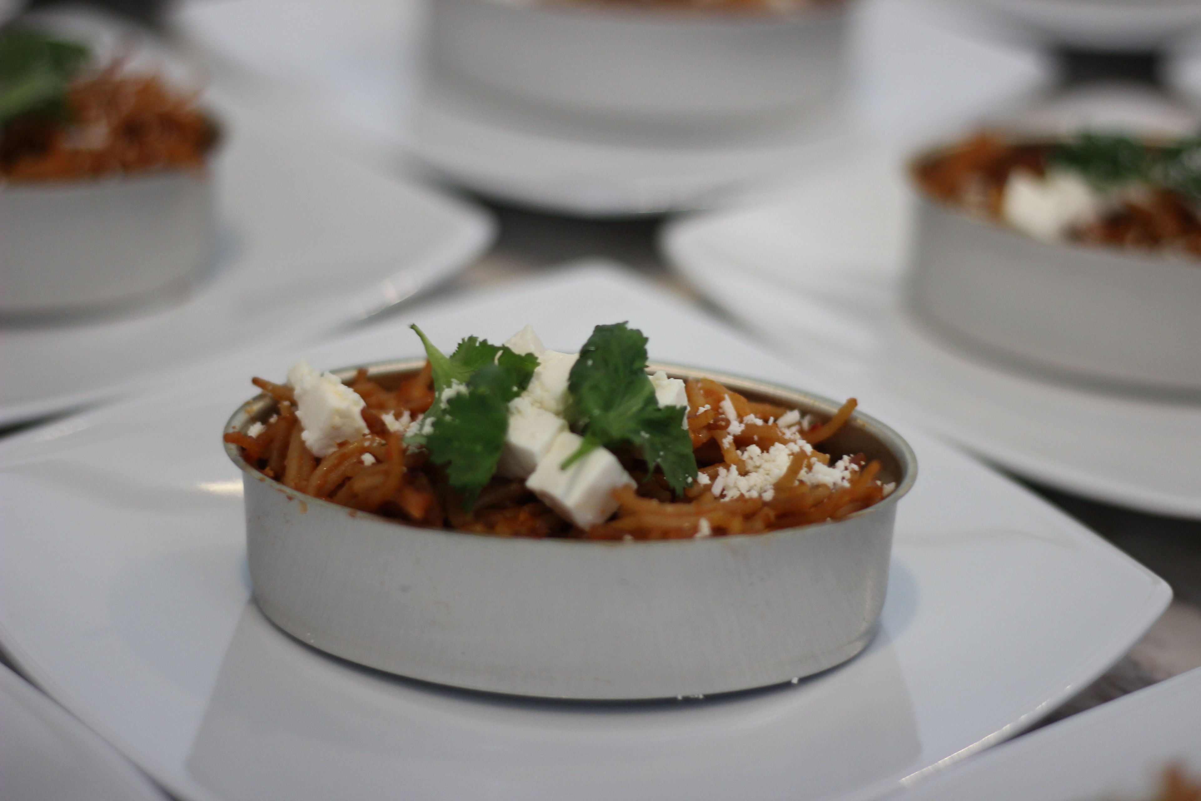 Une table à manger avec plusieurs assiettes blanches, chacune contenant un plat de pâtes, de fromage et d’herbes aromatiques.