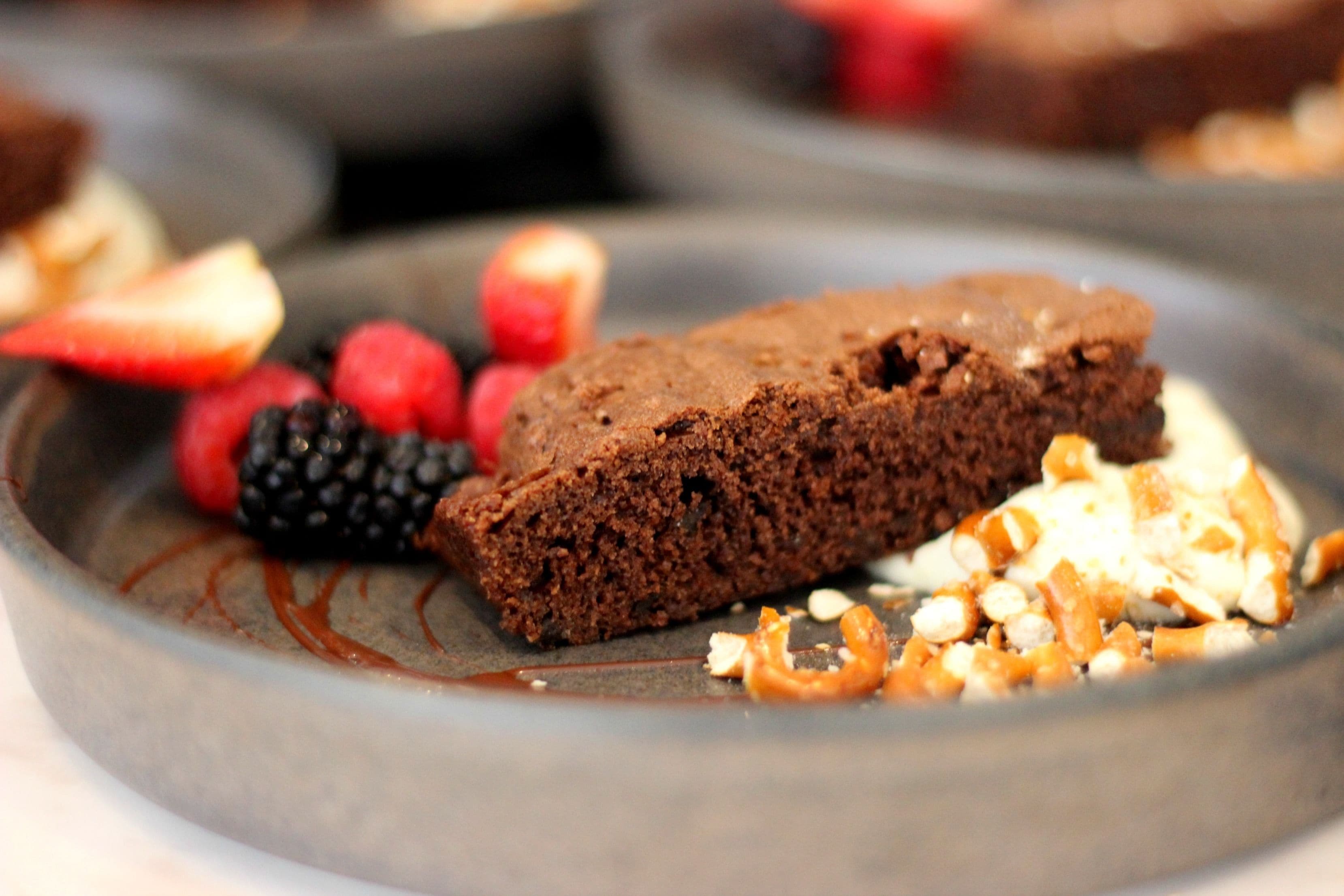 A dessert plate with a slice of chocolate cake, strawberries, raspberries, and nuts.