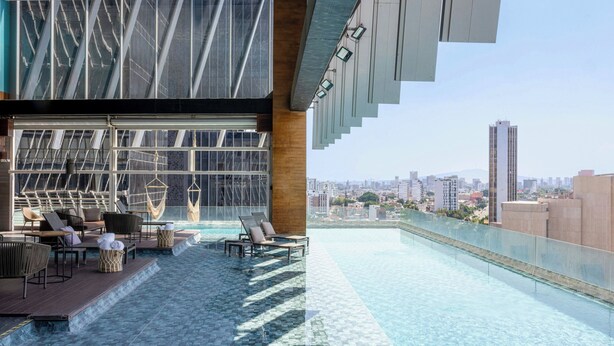 Una piscina infinita en la azotea con sillas de descanso, una terraza de madera y vistas a la ciudad.