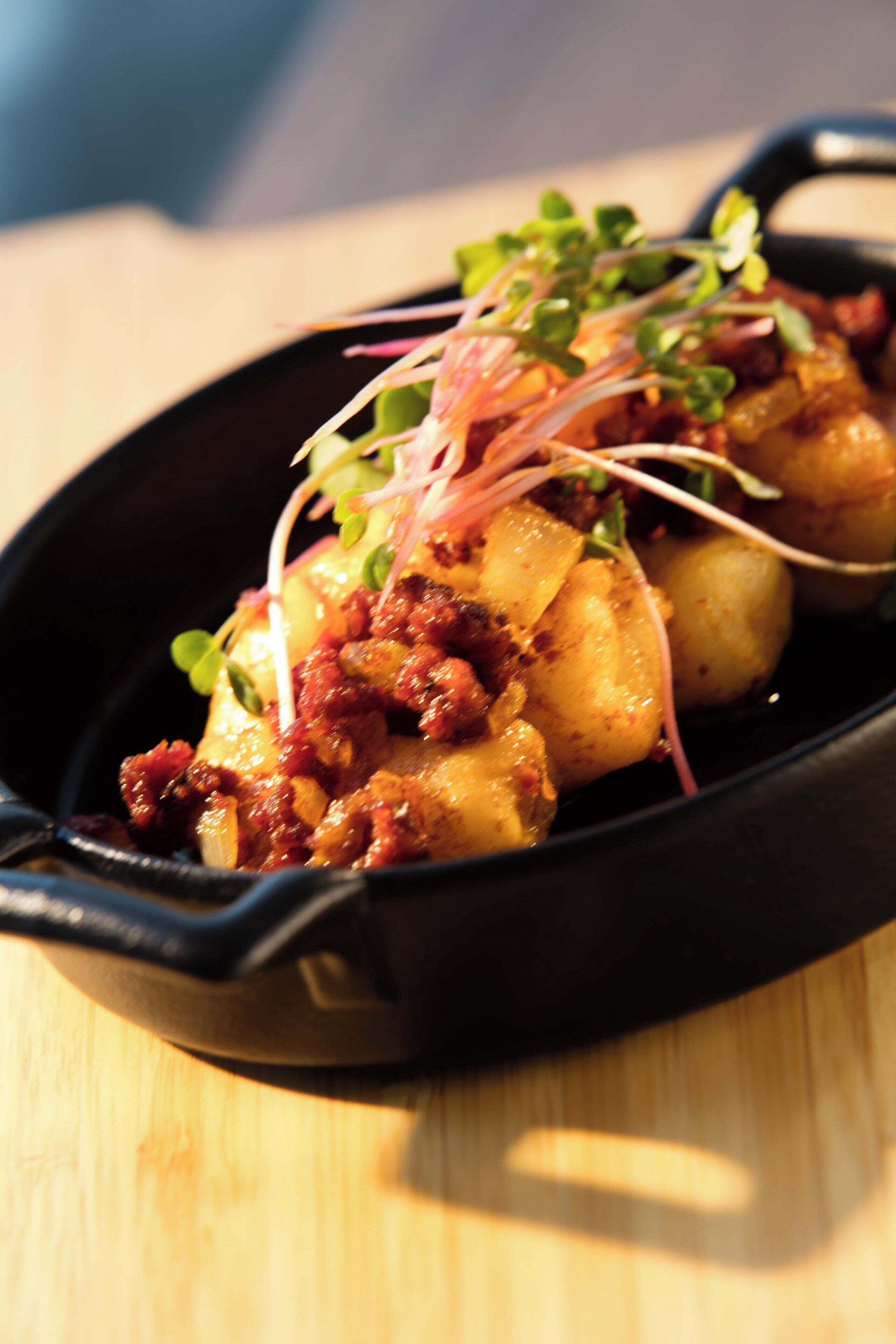 A skillet with food, possibly a dish with potatoes and meat, garnished with greens.