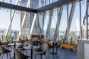Ein stilvoller Dachterrassen-Essbereich mit Tischen, Stühlen, großen Fenstern und Blick auf die Stadt.