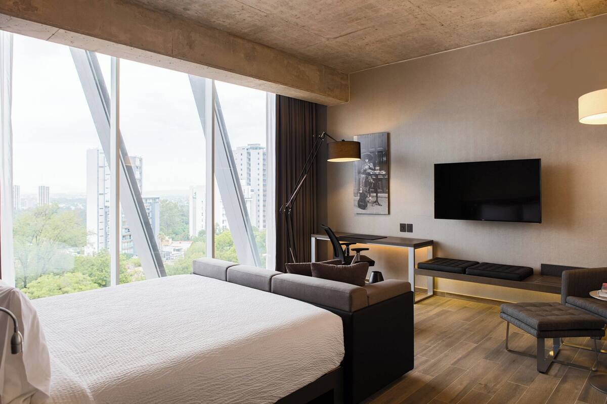 Una habitación de hotel moderna con una cama grande, un escritorio, un sofá y un televisor.