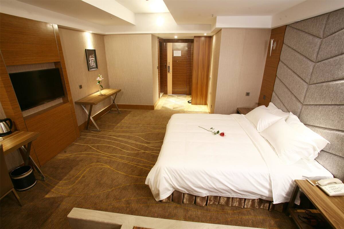 A hotel room with a large bed, a desk, a television, and a bathroom visible through an open door.