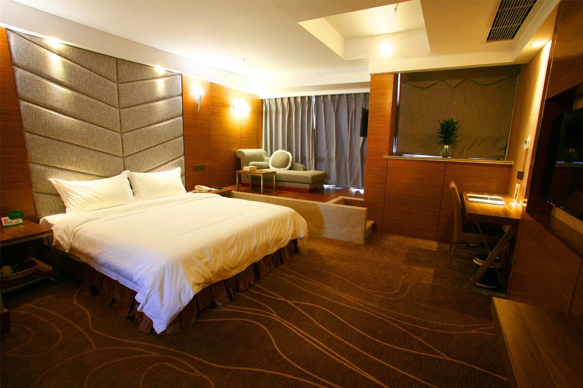 A hotel room with a large bed, a desk, a chair, a television, and a window with curtains.
