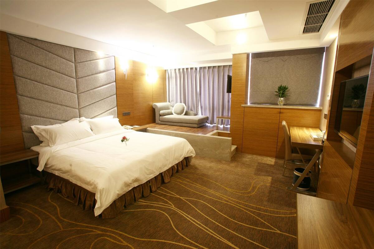 A hotel room with a large bed, a desk, a chair, and a TV.