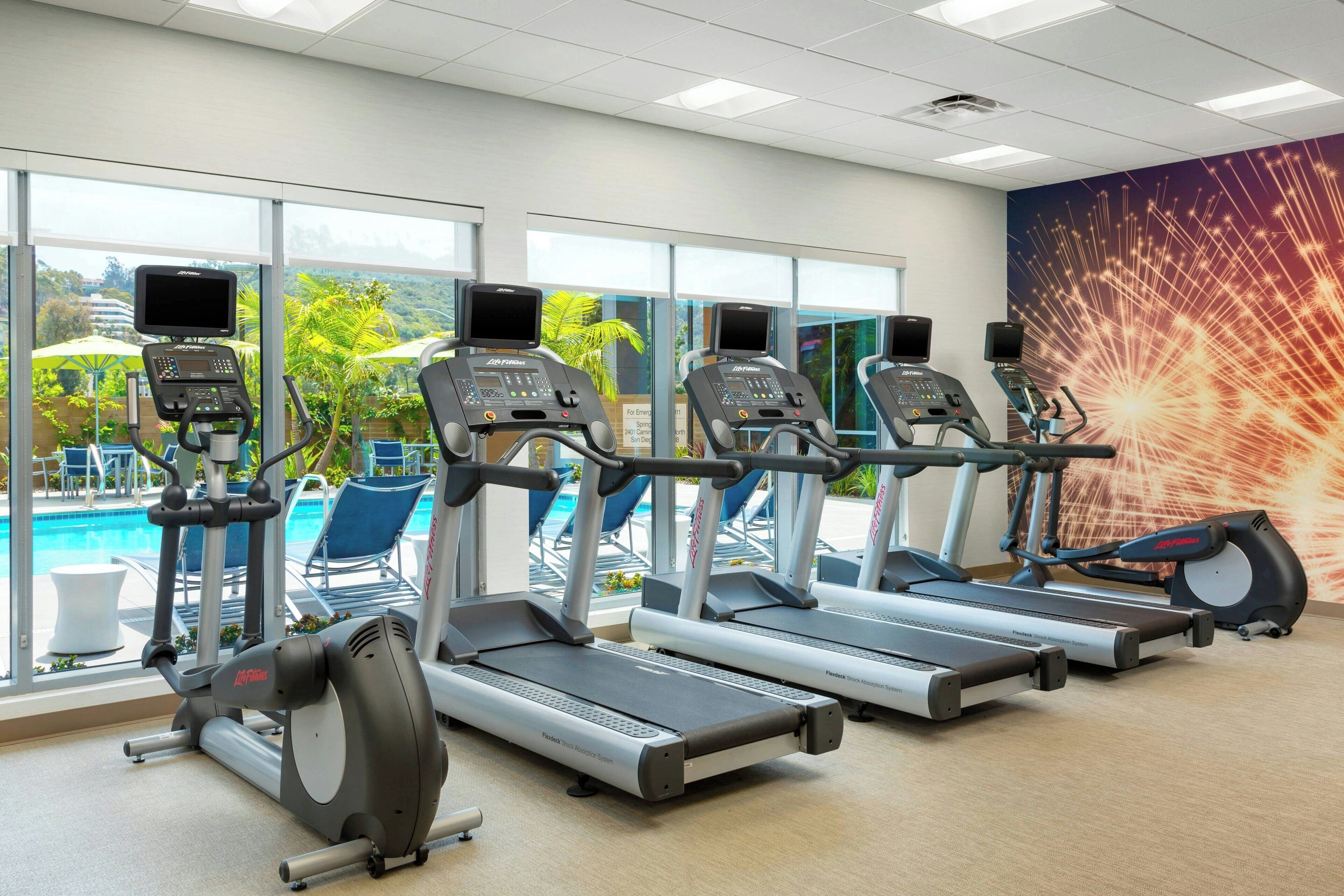 Gimnasio con cintas de correr, bicicletas estáticas y una zona de piscina visibles a través de amplios ventanales.