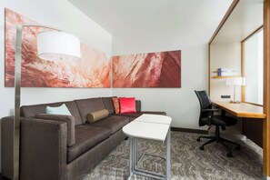 A modern hotel room with a sofa, a small table, a desk, and a chair. There are abstract paintings on the wall and a lamp on the floor. - Springhill Suites San Diego Mission Valley (San Diego)