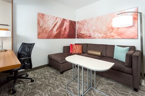 A modern hotel room with a brown sofa, a small white table, a black office chair, and two abstract paintings on the wall. - Springhill Suites San Diego Mission Valley (San Diego)