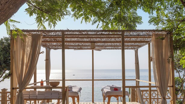 A wooden deck with two massage tables, a wooden bench, and a table with towels and a bowl.
