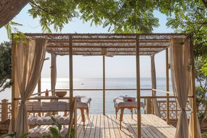 A wooden deck with two massage tables, a wooden bench, and a table with towels and a bowl. - Alua Calas de Mallorca Resort (Manacor)
