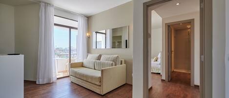 A spacious living area with a sofa, a dining table, and a large window with curtains.