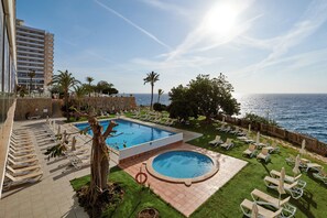 Ett poolområde vid semesteranläggningen med flera solstolar och en liten, rund pool, omgivet av palmer och med utsikt över havet.