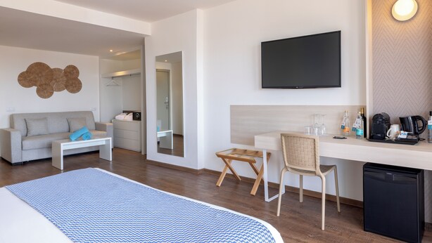 Una habitación de hotel moderna con una cama, un sofá, un escritorio con silla, un televisor y una cafetera.