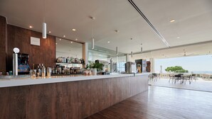 Un espace bar moderne avec un comptoir en bois, diverses bouteilles et une grande fenêtre donnant sur l’extérieur.
