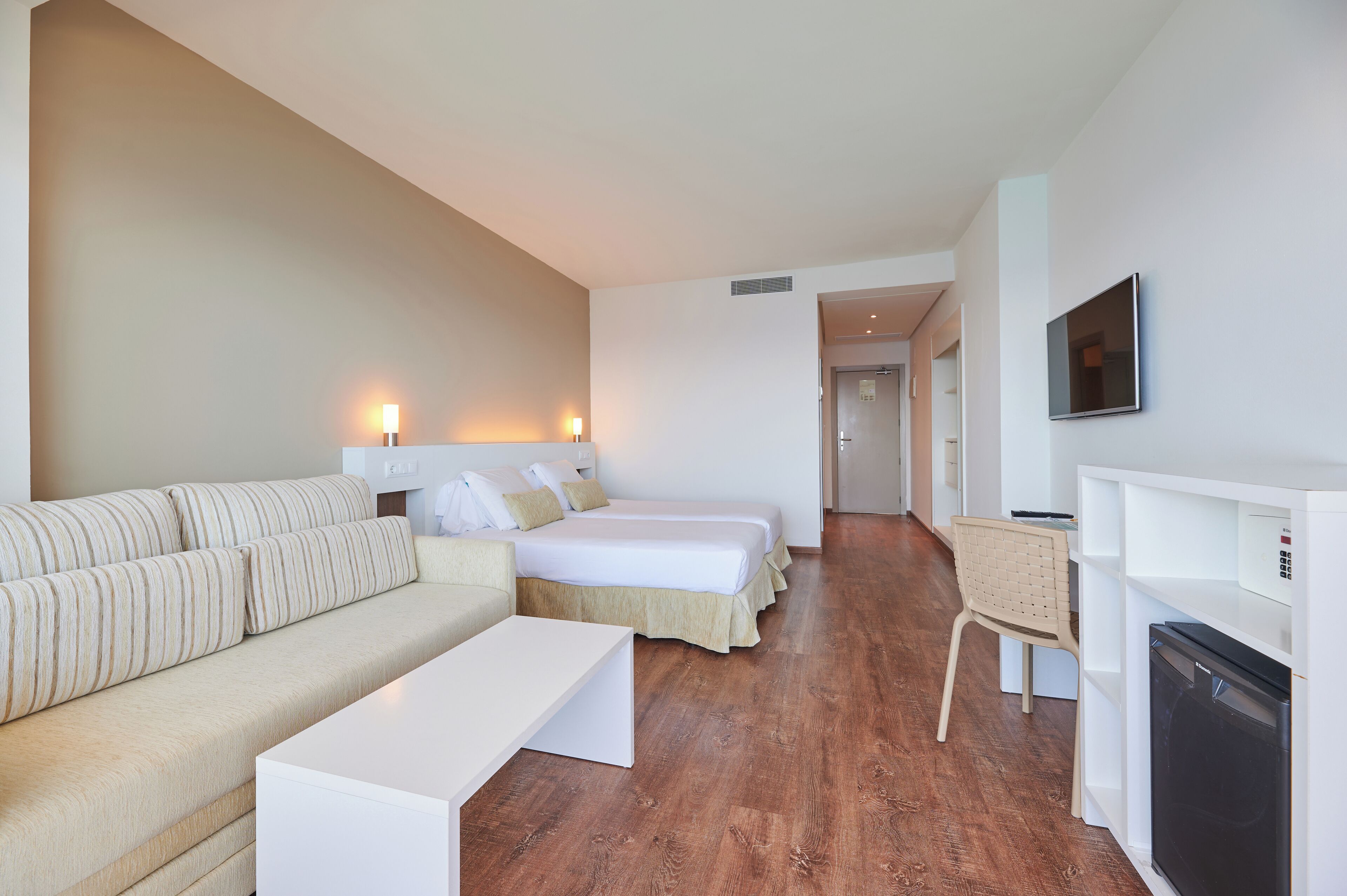 Camera d'albergo con divano, due letti, una scrivania, una TV e una lavatrice.