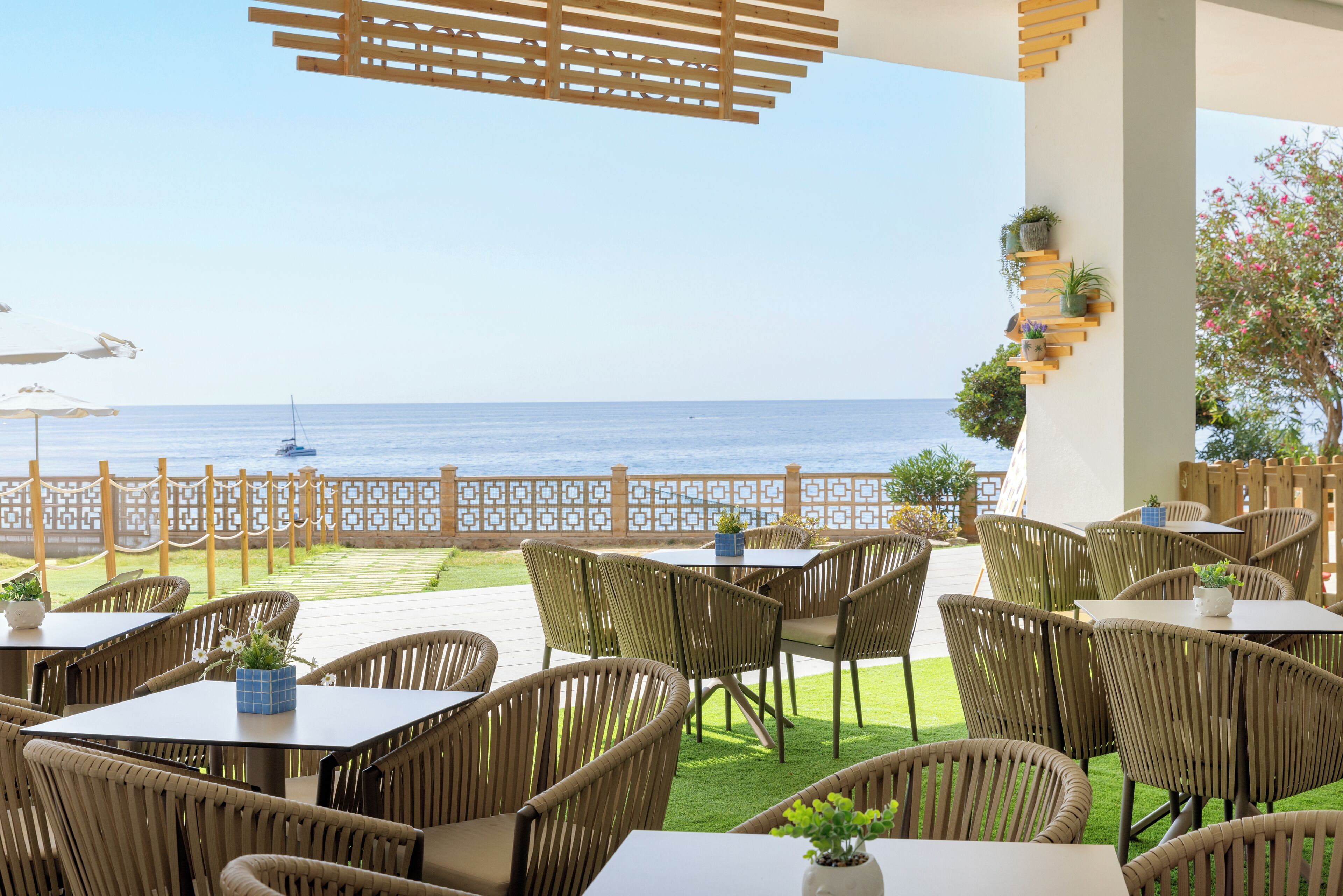 Eine Terrass mit Korbmöbeln, Blick auf das Meer und einem Holzzaun.