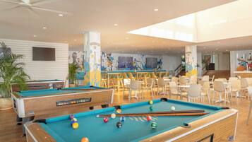 A pool area with multiple tables and chairs, a pool table, and a ceiling fan.