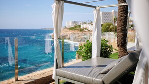 A beachside balcony with a glass railing, a white canopy, and a lounge chair.
