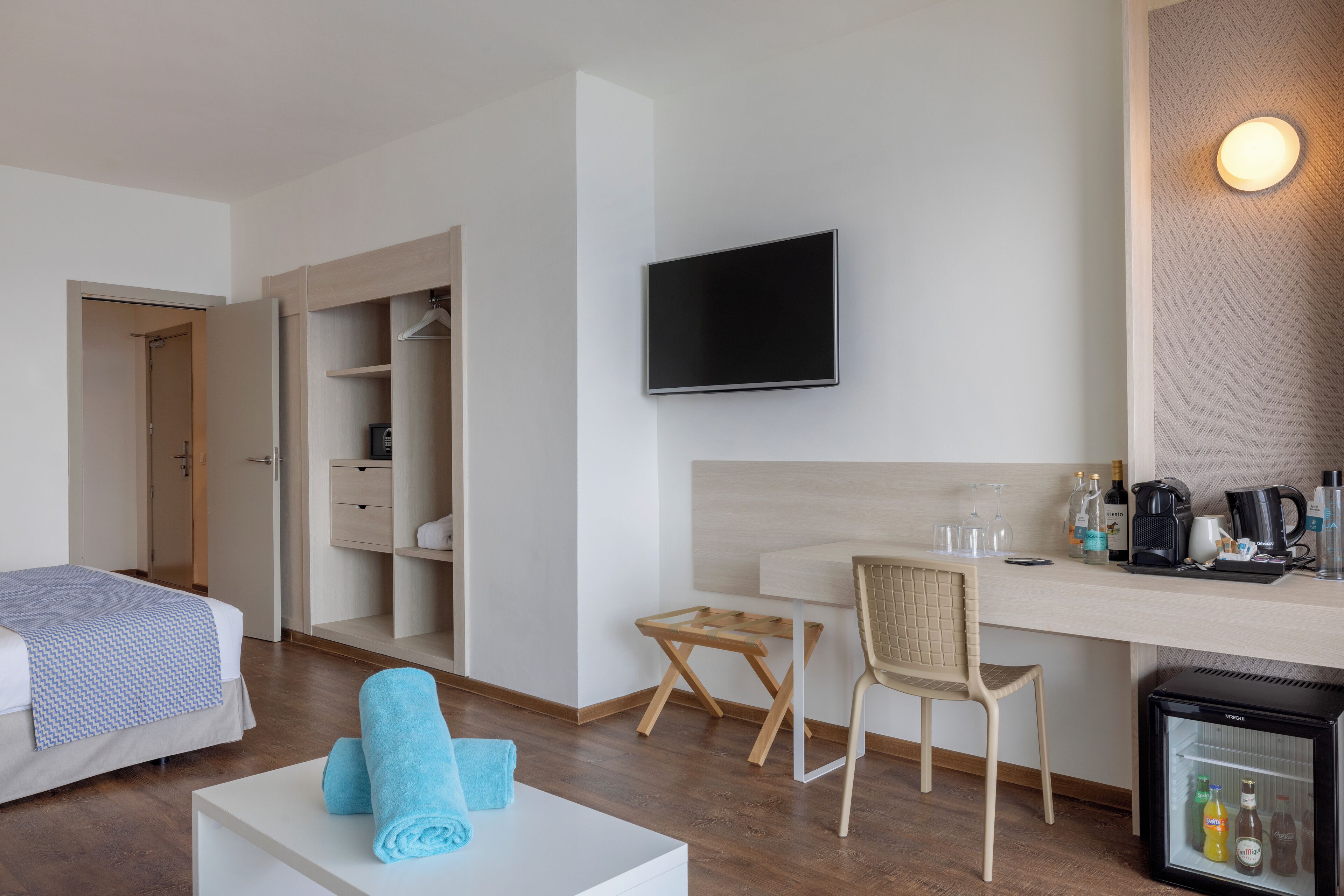 A hotel room with a bed, a desk, a chair, a television, and a minibar.