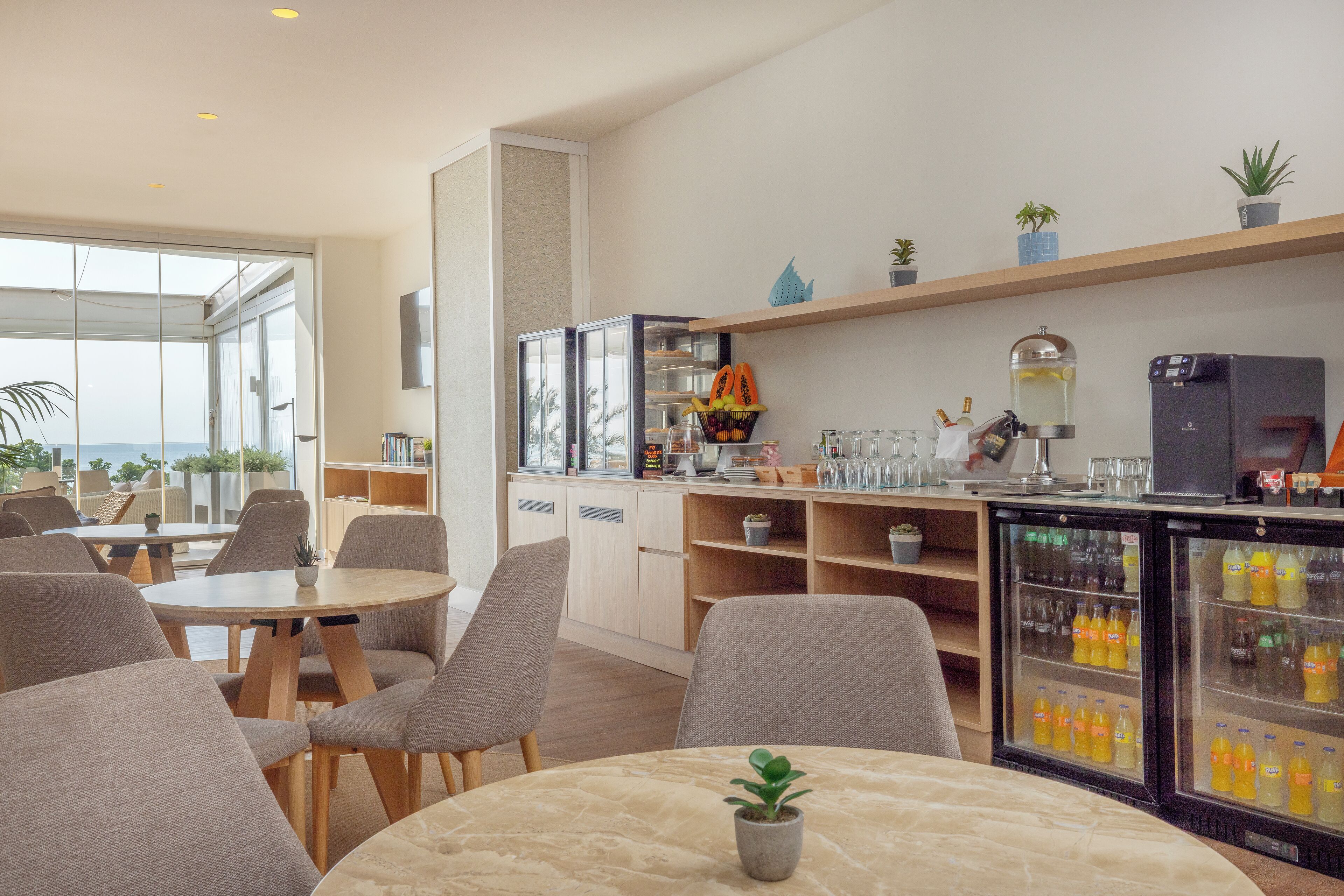 Un moderno vestíbulo de hotel con zona de estar, kitchenette y un refrigerador lleno de bebidas.