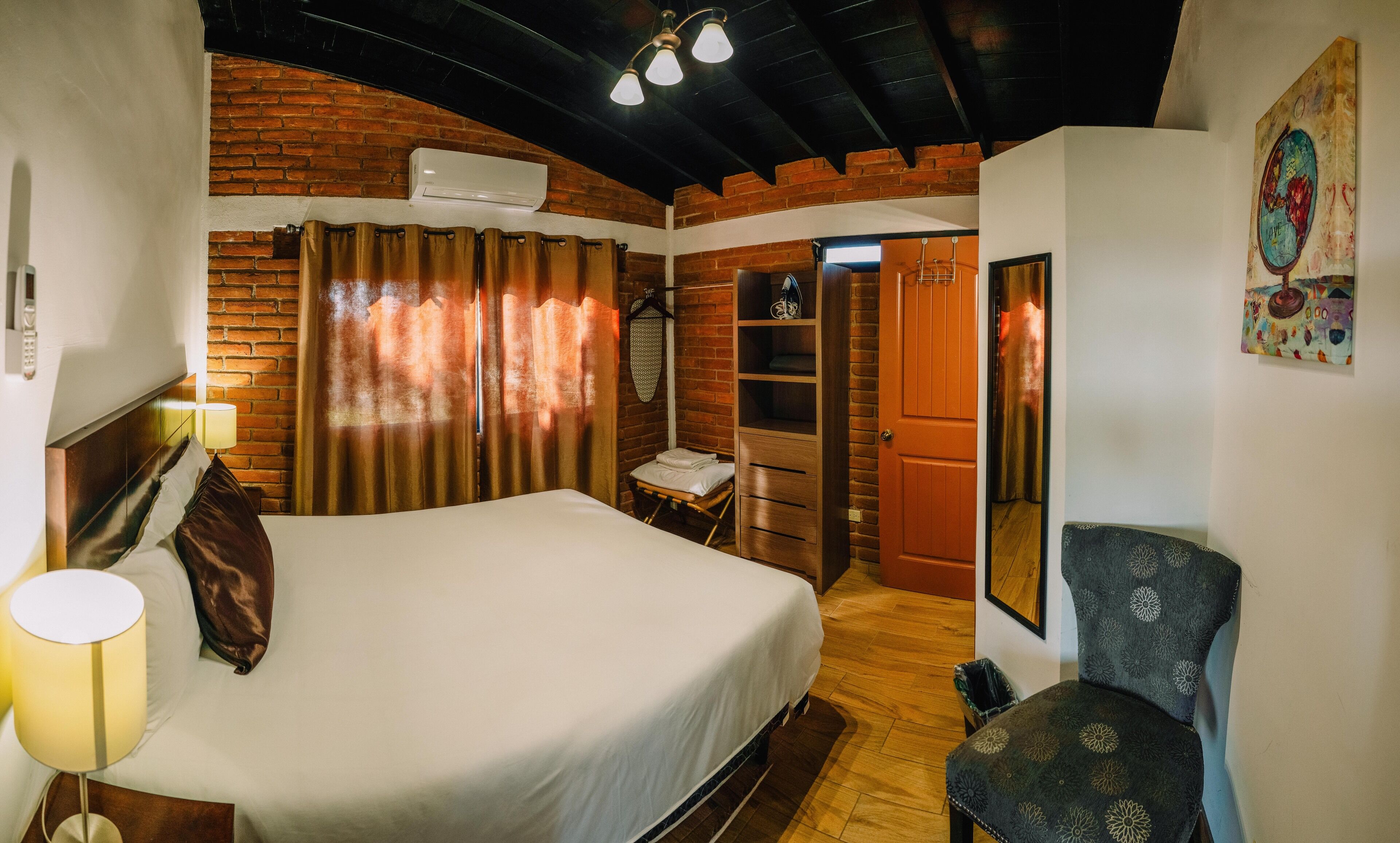 A hotel room with a bed, a chair, a wardrobe, and a bathroom visible through an open door.