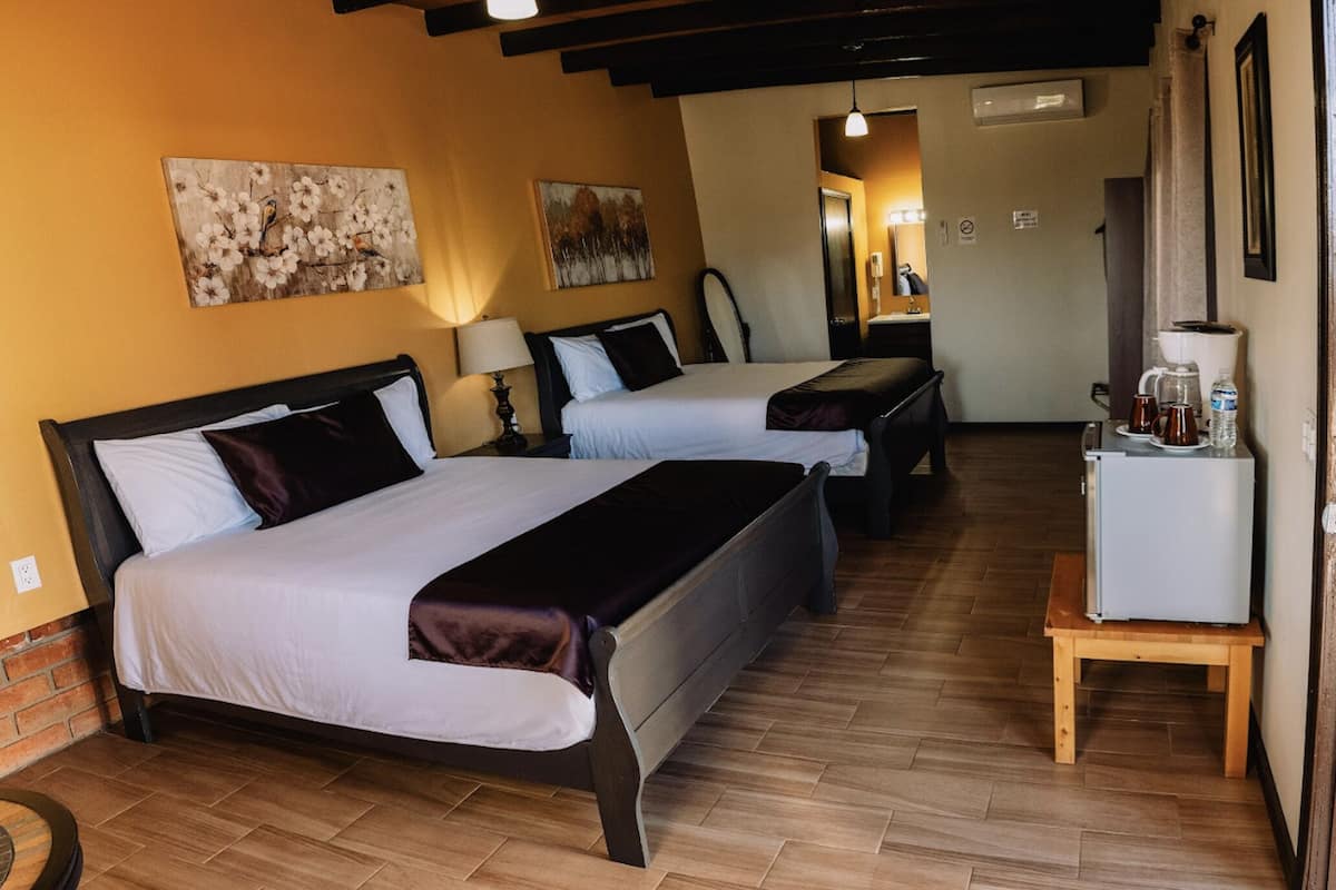 A hotel room with two beds, wooden flooring, and a small table with a coffee maker.
