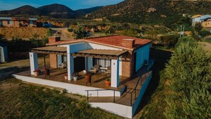 Una casa moderna con un patio, una zona de estar cubierta al aire libre y vistas a las colinas circundantes.