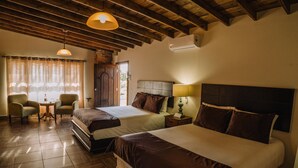 Una habitación de hotel con dos camas, techo de madera, ventana con cortinas y una pequeña mesa con sillas.