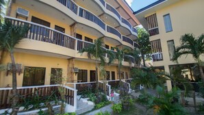 Un hotel de varios pisos con balcones, plantas exteriores y una escalera que lleva a la entrada.