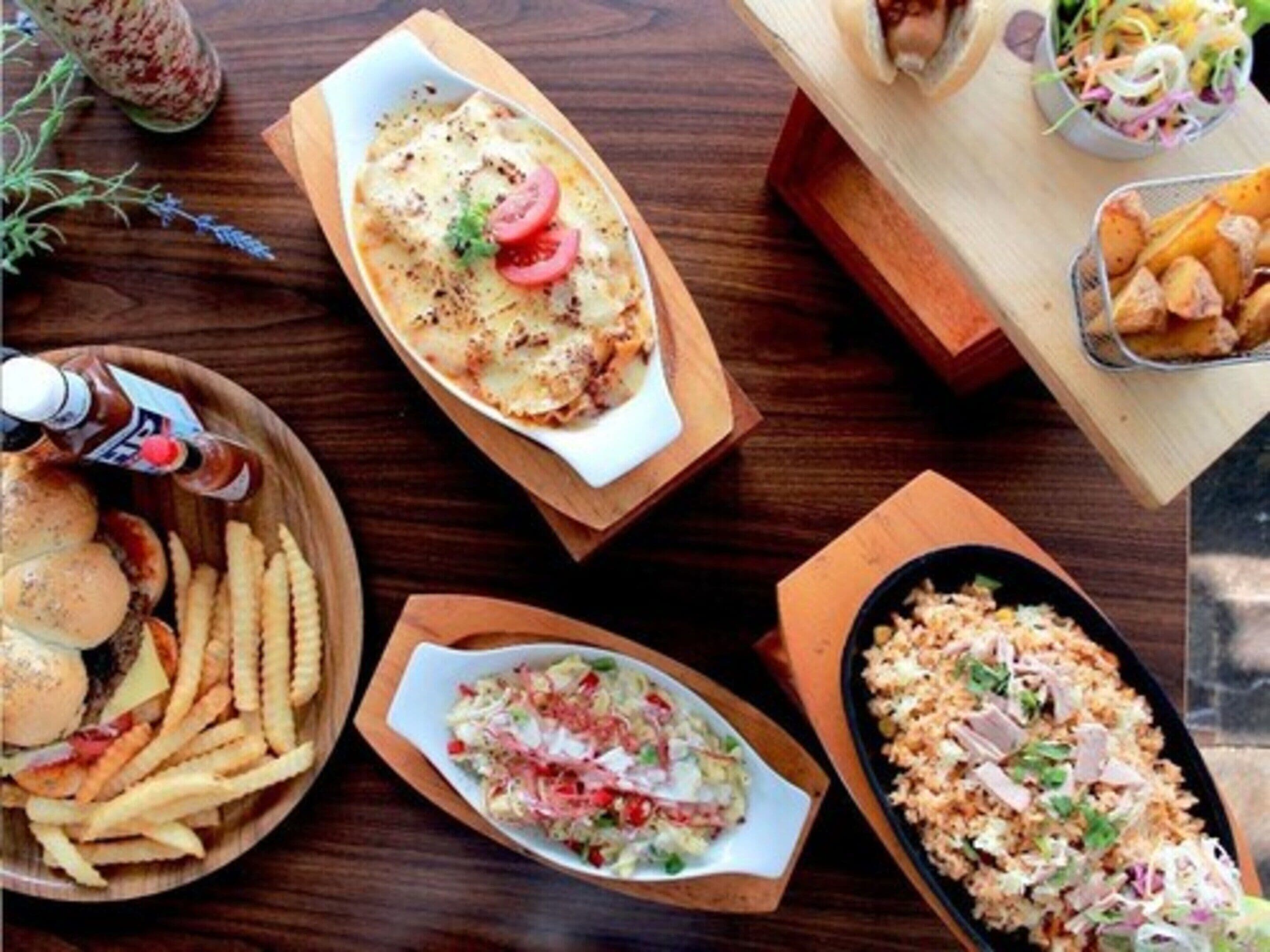 A table with various dishes including a baked dish with tomatoes, a salad, fries, and a rice dish with meat.